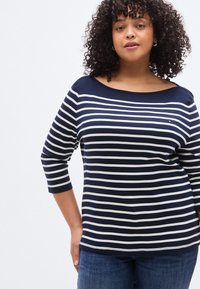 Κορυφή με λαιμόκοψη τύπου βάρκας σε μπλε ναυτικό και άσπρες ρίγες, με μανίκια τριών τετάρτων, κατασκευασμένη από απαλό ύφασμα. Διαθέτει μικρό λογότυπο στο μπροστινό μέρος.