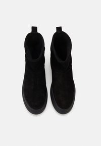 Schwarze Wildleder-Stiefeletten mit runder Zehenpartie, weicher Textur und Zuglasche hinten. Flache schwarze Gummisohle. Keine sichtbaren Metallteile.