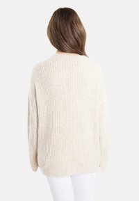Chunky stickad tröja i ljusbeige, med ribbad textur och avslappnad passform. Långa, vida ärmar och rundad halsringning.
