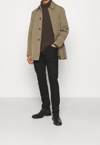 Světle hnědý kabát s límečkem, hnědý svetr, černé džíny a černé kotníkové boty. Kabát má velké knoflíky a uvolněný střih.