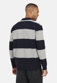 Pull en gris et bleu marine à rayures, avec une coupe décontractée. Col et poignets côtelés, texture douce et coutures visibles le long du dos.