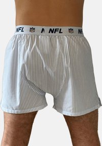 Weiße Herren-Boxershorts mit dünnen vertikalen blauen Streifen und einem mit dem NFL-Logo versehenen elastischen Bund am Unterkörper einer hellhäutigen Person.