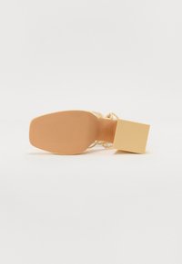 Sandal dengan pegang blok dan tumit persegi serta sol bertekstur, menampilkan desain terbuka dan warna beige terang. Tali sandal ramping dan saling silang.