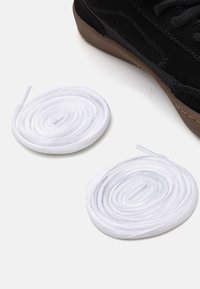Two white round shoelaces, textured, next to a black suede sneaker with a brown rubber sole.