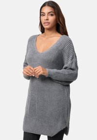 Pull en maille grise avec col en V, manches longues et tissu texturé. Présente une coupe décontractée et des fentes latérales pour plus de style.