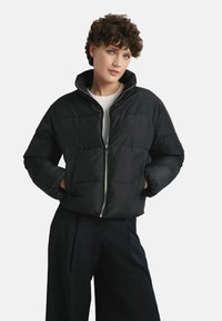 Czarna kurtka puchowa z wysokim kołnierzem, zapinana na zamek z przodu, z dwoma bocznymi kieszeniami. Posiada pikowany wzór i krótki krój.