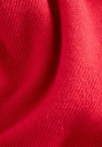 Tessuto a maglia rosso con una superficie liscia, caratterizzato da un motivo a coste che aggiunge profondità e tridimensionalità. Il colore è vibrante e uniforme.