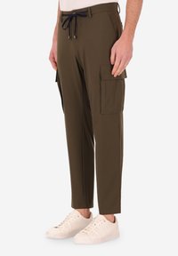 Pantaloni cargo verde oliva con vita regolabile, dotati di tasche laterali e taglio affusolato, abbinati a sneakers bianche.