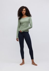 Lichtgroene lange mouwen top met een ronde hals, gecombineerd met fitted marineblauwe leggings. Beide kledingstukken zijn gemaakt van een zachte, rekbare stof.