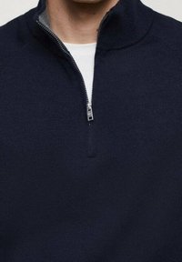 Pull zippé marine avec col montant, featuring a silver zipper, des poignets côtelés et une texture tricot lisse.
