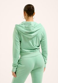 Completo athleisure verde menta con giacca con cappuccio e pantaloni aderenti, realizzato in tessuto morbido e con dettagli di cucitura minimi.