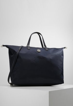 Grand sac cabas en nylon noir avec double poignée, bandoulière amovible et logo métallique circulaire au centre avant.