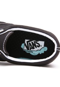Musta kankaiset tennarit, joissa on valkoinen reuna. Ominaisuuksiin kuuluu "VANS ComfyCUSH" -logo vaaleansinisellä taustalla, jota ympäröi musta pistekuvio.
