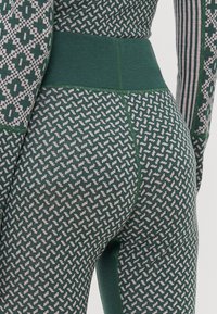 Leggings verdes con un patrón que presentan una cinturilla alta. La tela tiene un tejido texturizado con pequeñas formas geométricas en un color más claro.