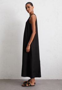 Abito maxi senza maniche di colore nero con una silhouette rilassata, realizzato in tessuto morbido, caratterizzato da un orlo lungo fino al pavimento e semplici elementi di design.