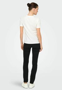 Camiseta blanca de manga corta combinada con pantalones ajustados negros y zapatillas blancas. Material de algodón suave con un diseño clásico de cuello redondo.
