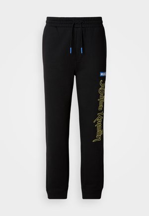 Zwarte joggingbroek met elastische tailleband en trekkoord, voorzien van een blauw label en een gele "Jujutsu Kaisen" graphic op het linkerpijp.