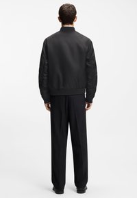 Black bomber jacket with a textured fabric and ribbed collar, paired with tailored black trousers, viewed from the back.