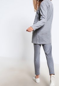 Felpa grigia e pantaloni abbinati realizzati in un tessuto morbido. I pantaloni sono slim-fit e la felpa ha un taglio dritto con tasche. Sneakers bianche.