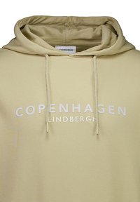Felpa beige con testo bianco frontale "COPENHAGEN LINDBERGH" e lacci che pendono dall'apertura del cappuccio.