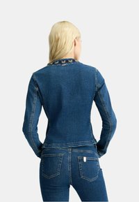 Giubbotto in denim con un design aderente, di colore azzurro chiaro, maniche lunghe e colletto decorativo. Presenta cuciture classiche e due tasche posteriori.