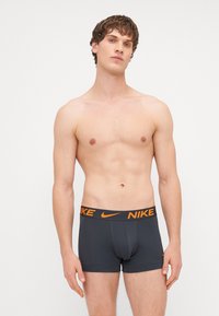 Crne bokserice s narančastim Nike logom na pojasu. Izrađene od rastezljivog materijala, s uskim prilagodbom i glatkom teksturom.