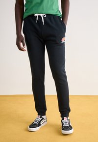 Svarta träningbyxor med elastisk midja och justerbar dragsko, med en liten logotyp på låret. Tillsammans med mönstrade svarta sneakers.