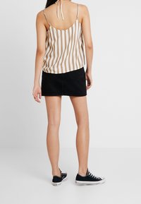 Camisole rayé en beige et blanc, avec des bretelles réglables, associé à une mini-jupe en denim noir et des baskets en toile noires.