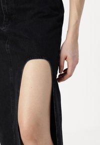 Saia de ganga preta com uma fenda alta do lado esquerdo, revelando pele. O tecido tem um leve brilho e é ajustado ao corpo.