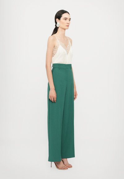 Hvit satin cami med blonder, kombinert med høy midje grønne vide bukser og beige høyhælte sandaler.