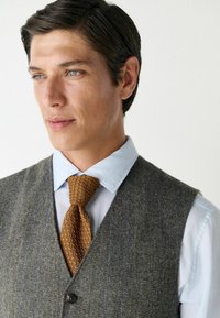 Gray herringbone vest over a light blue shirt, complemented by a textured brown tie. Smooth fabric with defined patterns and accents.