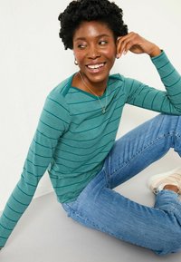 Langärmliges, türkis gestreiftes Oberteil mit Rundhalsausschnitt, kombiniert mit hellblauen Jeans und beigen Sneakers, in einer lockeren Passform.