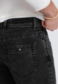 Svarta denimjeans med en urtvättad finish, med en bakficka med metallknapp och en "ombre denim" etikett på midjebandet.