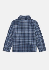 Blå rutete skjorte med lange ermer og krage. Laget av mykt materiale med et sjakkmønster i ulike nyanser av blått og hvitt.