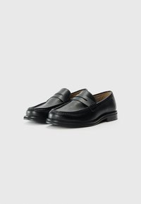 Mocassins en cuir noir avec un bout arrondi, une sangle décorative sur le coup de pied et un petit talon solide. Texture lisse et design traditionnel.