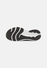 Semelle de chaussure avec un motif de traction en caoutchouc noir, présentant des accents blancs et une surface texturée pour l'adhérence et la flexibilité.