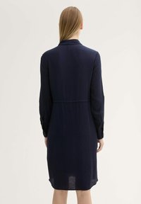 Abito blu navy con taglio diritto, maniche lunghe e cucitura visibile in vita. Realizzato in materiale leggero, con polsini abbottonati.