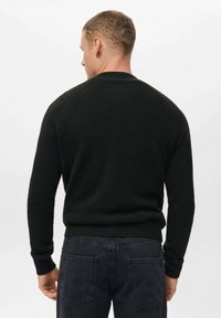 Maglione nero in maglia con scollo a giro e polsini a costine, dal tessuto morbido e dalla vestibilità aderente. Indossato con jeans scuri.