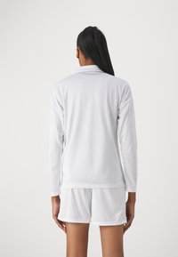White long-sleeve athletic top and matching shorts, made of smooth, lightweight fabric, featuring a classic collar and clean seams.
