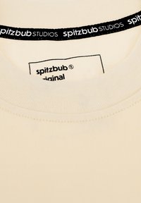 Cream-colored t-shirt with a ribbed crew neckline. Features a black label with "spitzbub STUDIOS" and "original" in white text inside the collar.