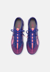 Scarpe da ginnastica viola e rosa con una parte superiore testurizzata, lacci in contrasto e un design aerodinamico. Caratterizzate da un tallone rinforzato e una linguetta imbottita.