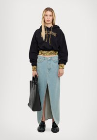 Felpa nera con testo dorato, cintura decorata. Gonna in denim azzurro chiaro con spacco frontale. Borsa tote nera e scarpe chunky nere completano il look.