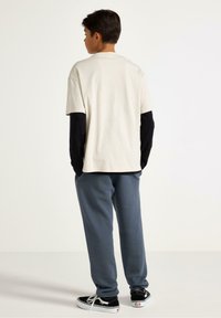 Lichtbeige t-shirt met korte mouwen over een zwart shirt met lange mouwen, gecombineerd met blauwe joggingbroek en zwarte sneakers. Eenvoudig en casual ontwerp.