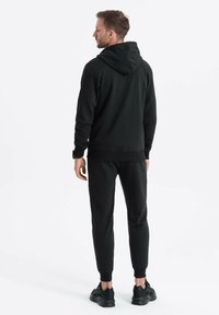 Sort hættetrøje og matchende joggers lavet af blødt stof, med en afslappet pasform, lange ærmer, en hætte og ribbet manchet og talje.