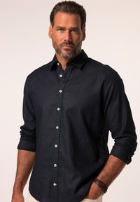 Camicia blu navy con bottoni, realizzata in lino con una texture liscia, maniche lunghe arrotolate fino ai gomiti e bottoni bianchi per la chiusura.