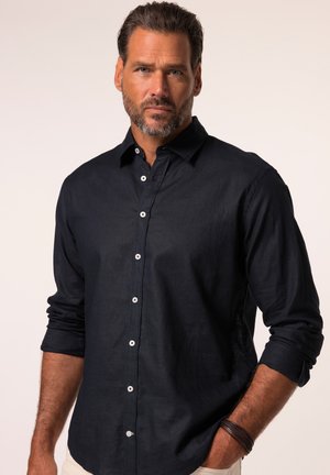Navyblaue Button-Down-Hemd aus Leinen mit glatter Textur, langen Ärmeln, die bis zu den Ellenbogen gerollt sind, und weißen Knöpfen zum Schließen.