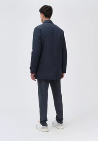 Giacca della Marina con colletto, maniche lunghe e bottoni; abbinata a pantaloni scuri e sneakers bianche con accenti arancioni.