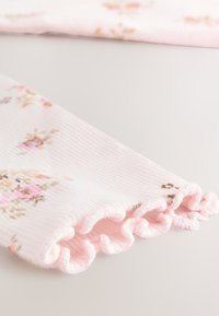 Ribbed pink fabric with small floral patterns, featuring ruffled edges. Soft texture, mainly pastel colors with hints of brown, pink, and blue.