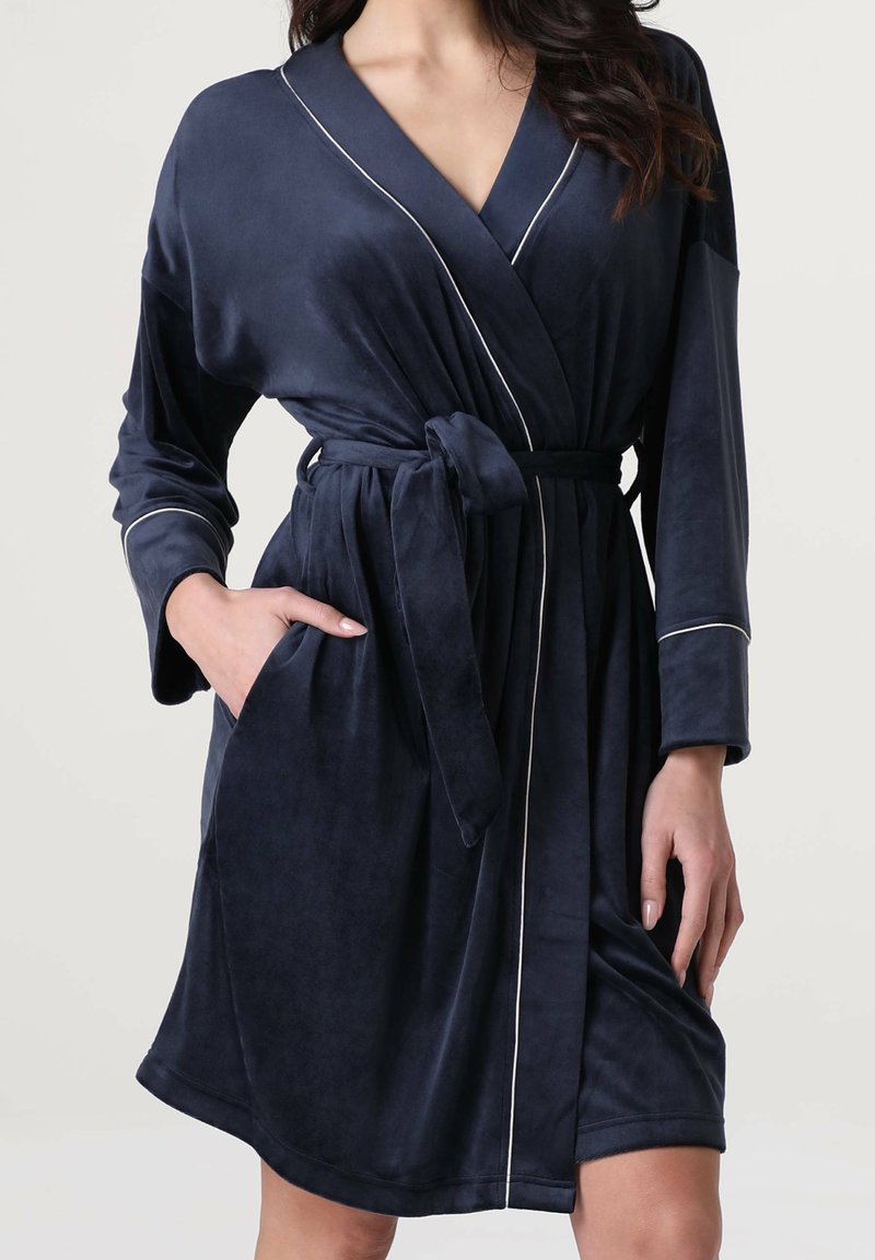 Accappatoio in peluche blu navy con colletto a scialle, piping bianco, cintura e tasche laterali. Tessuto morbido e design al ginocchio.