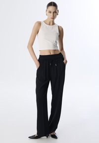 Biała bezrękawnikowa bluzka crop top z okrągłym dekoltem, zestawiona z czarnymi szerokimi spodniami z elastycznym pasem i bocznymi kieszeniami. Czarne czółenka.